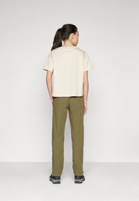 Beige katoenen T-shirt met korte mouwen, gecombineerd met olijfgroene, strakke broeken. De outfit heeft een eenvoudig, strak ontwerp zonder zichtbare patronen.