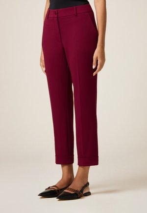 Pantalons taillés bordeaux avec une texture lisse, dotés de poches latérales et d'un design à revers, associés à des ballerines noires et tan.