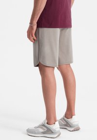 Pantalones cortos deportivos de color gris claro con una textura suave, con dobladillos redondeados. Combinados con zapatillas deportivas blancas y grises. Se puede ver una camiseta de color granate.