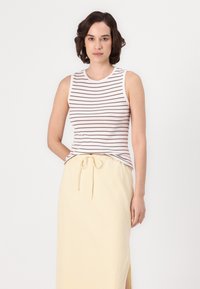 Haut sans manches blanc avec des rayures horizontales marron, associé à une jupe maxi jaune avec une taille à cordon et une fente sur le côté.