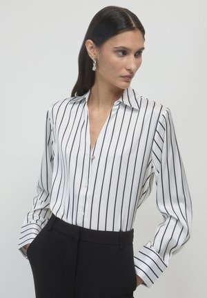 White blouse with black vertical stripes, collared neckline, button placket, and long sleeves; worn with black trousers. Smooth texture.