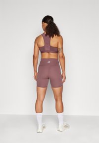 Fialová sportovní podprsenka a odpovídající šortky vyrobené z elastického materiálu. Obsahuje design s racerback a logo na pásku.