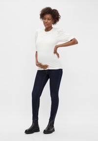 Top blanco de manga abullonada con cuello de encaje, combinado con jeans ajustados de mezclilla oscura y botas negras de tobillo con cremalleras en los tobillos.