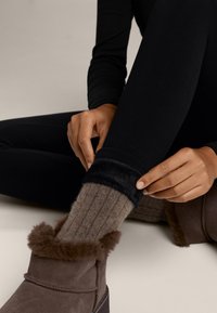 Zwarte strakke leggings met een zachte zwarte nepbont manchette, gecombineerd met een tan ribbel sok en een bruine suède laars met een harige bovenrand.