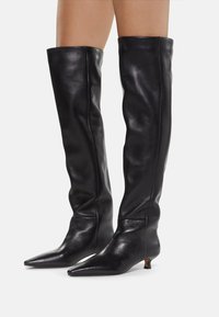 Knee-high black leather boots with a pointed toe and a low angled heel. The upper has a smooth texture and a fitted silhouette.