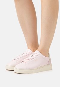 Helle rosa Leder-Sneaker mit weißer Sohle, ausgestattet mit Schnürsenkeln, dezentem Branding und einem Absatz in neutralen Farben. Glatte Textur.