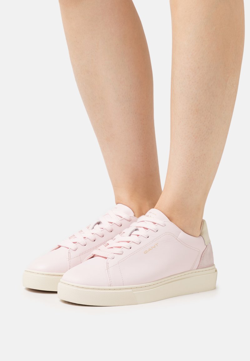 Helle rosa Leder-Sneaker mit weißer Sohle, ausgestattet mit Schnürsenkeln, dezentem Branding und einem Absatz in neutralen Farben. Glatte Textur.