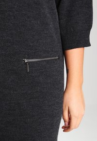 Robe en maille gris foncé avec une poche zippée sur le côté gauche, dotée de poignets côtelés et d'une texture douce.