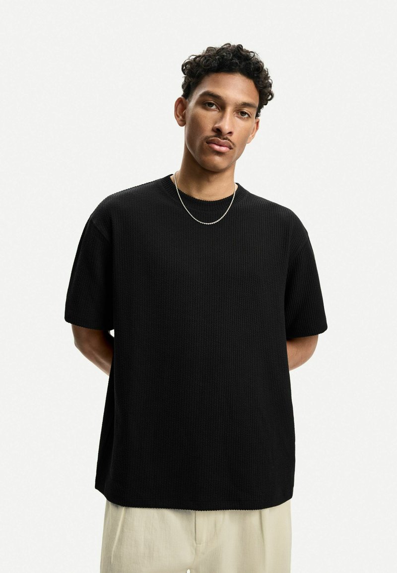 Črna majica s kratkimi rokavi z teksturiranim materialom, udobnim krojem, okroglim ovratnikom in gladkim, minimalističnim dizajnom.