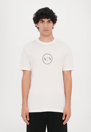 Camiseta blanca de algodón con mangas cortas, que presenta un logotipo circular negro con "A" y "X" en el centro. Diseño sencillo de cuello redondo.