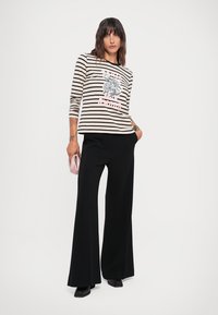 Striped long-sleeve top in beige and black with floral print; paired with black wide-leg trousers and a small pink clutch.