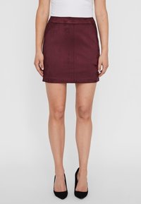 Bordowa mini spódnica o gładkiej fakturze, dopasowanym kroju i prostym końcu. Stylizowana z białą bluzką i czarnymi szpilkami.