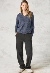 Marineblauw longsleeve met een bladerenpatroon, gecombineerd met donkergrijze, loszittende broek. Schoeisel zijn witte sneakers.