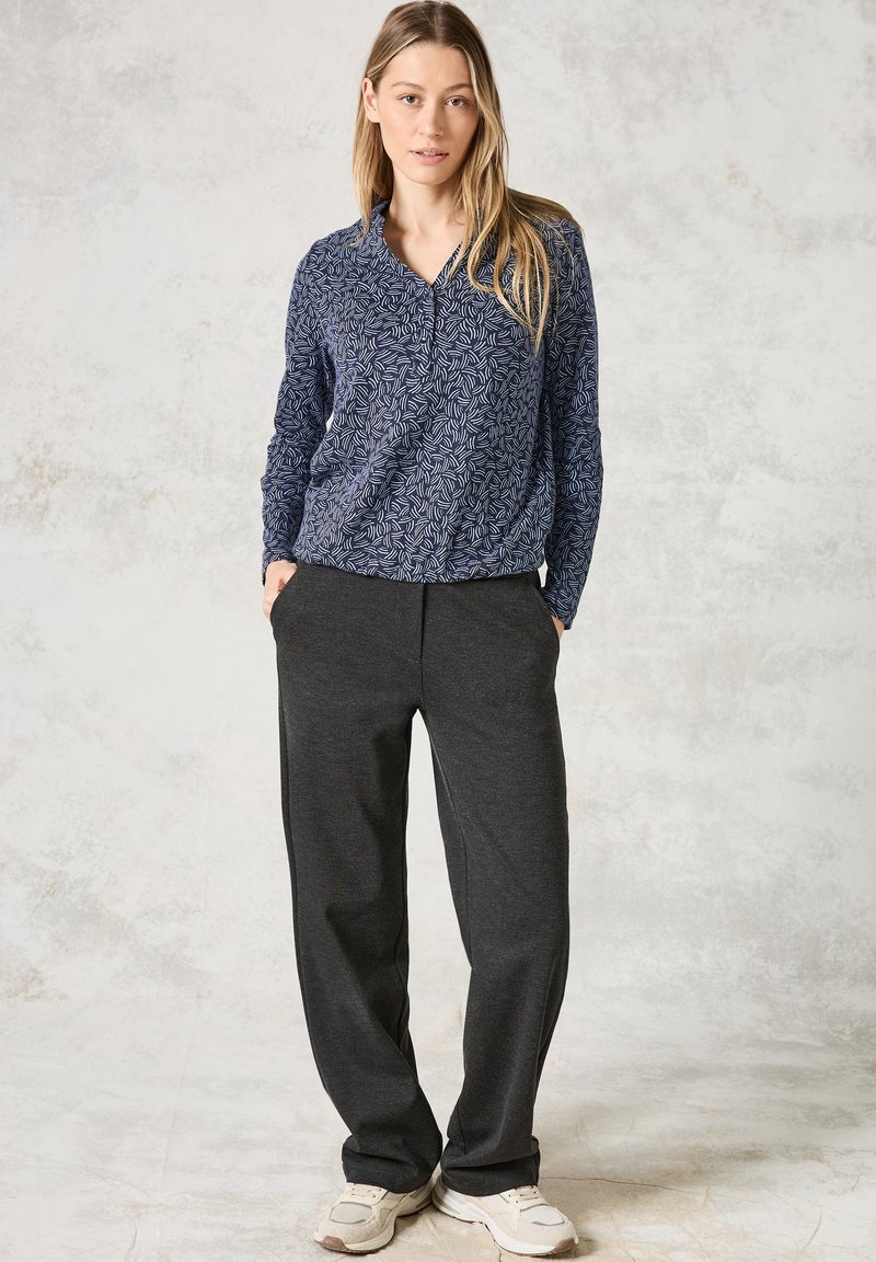 Marineblauw longsleeve met een bladerenpatroon, gecombineerd met donkergrijze, loszittende broek. Schoeisel zijn witte sneakers.