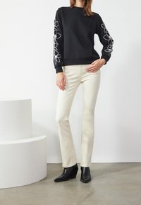 Svart sweatshirt med vit blommig brodyr på ärmarna, parat med ljusbeiga raka jeans och svarta klackade ankelboots.