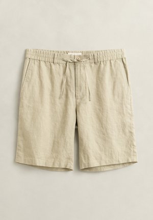 Beige legere Shorts in knielanger Länge mit elastischem Bund, Kordelzug, Knopfverschluss und Seitentaschen, flach auf hellem Hintergrund ausgelegt.