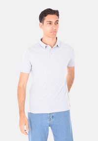 Polo shirt grigio chiaro a maniche corte con colletto, pattina con due bottoni e una texture morbida. Abbinato a jeans in denim blu chiaro.