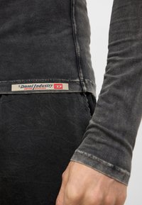 Čierna košeľa s dlhým rukávom s vyblednutou textúrou. Obsahuje viditeľnú nášivku Diesel Industry blízko spodného lemu a priliehavý dizajn rukáva.