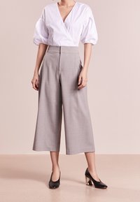 Top bianco avvolgente con maniche a sbuffo abbinato a culotte grigie a vita alta. Tacchi neri con tacco a blocco metallico completano l'outfit.