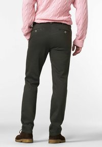 Pantalons verts foncés à coupe slim, dotés de deux poches arrière avec des fermetures éclair et d'une texture lisse. Associés à un pull en tricot à mailles torsadées rose clair.