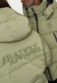Grønne puff jackets med en glat tekstur prydes af et stort "MULTIPLY APPAREL" print og mindre logo accenter, designet til varme og stil.