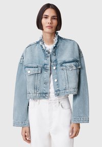 Chaqueta de mezclilla azul recortada con cuello deshilachado, bolsillos frontales y detalles de metal plateado. Tejido texturizado con un ajuste casual.