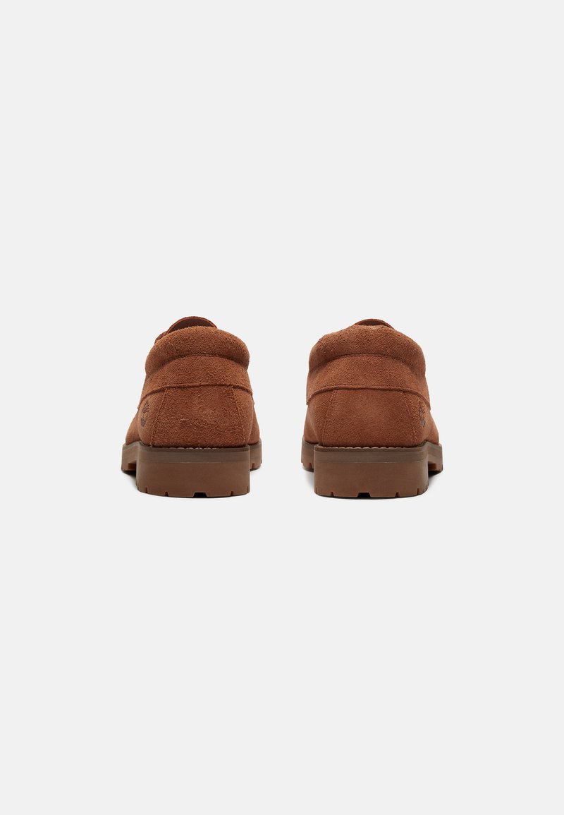 Scarpe in camoscio marrone con forma arrotondata, dotate di colletto imbottito e suola texturizzata per una migliore aderenza. Cuciture minime e dettagli del logo sul lato.