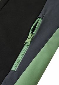 Schwarzer und grüner Reißverschlussstoff-Bereich mit kontrastierender Textur; verfügt über einen glatten Reißverschluss mit einem grünen Zugband entlang der Naht.