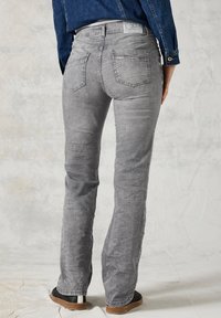 Grijze denim jeans met een rechte pasvorm, met een subtiele vervaagde textuur en twee achterzakken. Gedragen met een blauwe denim top en zwarte schoenen.