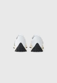 Baskets de sport blanches avec une semelle extérieure en caoutchouc noir texturé et des accents verts, dotées d'un dessus en synthétique lisse et d'un col rembourré pour le confort.