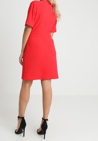 Röd klänning med korta ärmar, figurnära passform, knälång slut, gjord av slätt tyg. Matchad med svarta högklackade skor med ankelremmar.