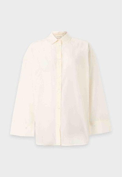 Chemise blanche à manches longues avec boutons, col classique et poignets, présentée sur un fond clair uni.