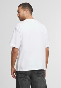Hvid bomulds t-shirt med korte ærmer og lige skæring, med rund halsudskæring og minimalistisk design, set fra ryggen.
