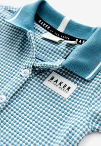 Modrá polo košeľa so vzorom, ktorá má textúrovaný dizajn, golier na dva gombíky a bielu etiketu s čiernym textom "BAKER by TED BAKER."