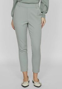 Vaaleanharmaat kapenevat housut, joissa on sileä kangas, korkea vyötärö ja sivutaskut. Yhdistettyinä kermaiseen kenkäpariin, jossa on mustia yksityiskohtia.