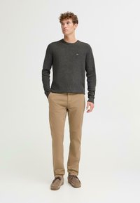 Musta harmaa neulepaita, beige puuvillahousut ja vaaleanruskeat kengät. Yksinkertainen muotoilu, jossa on pyöreä kaula-aukko ja huomaamaton brändilogo neulepaidassa.