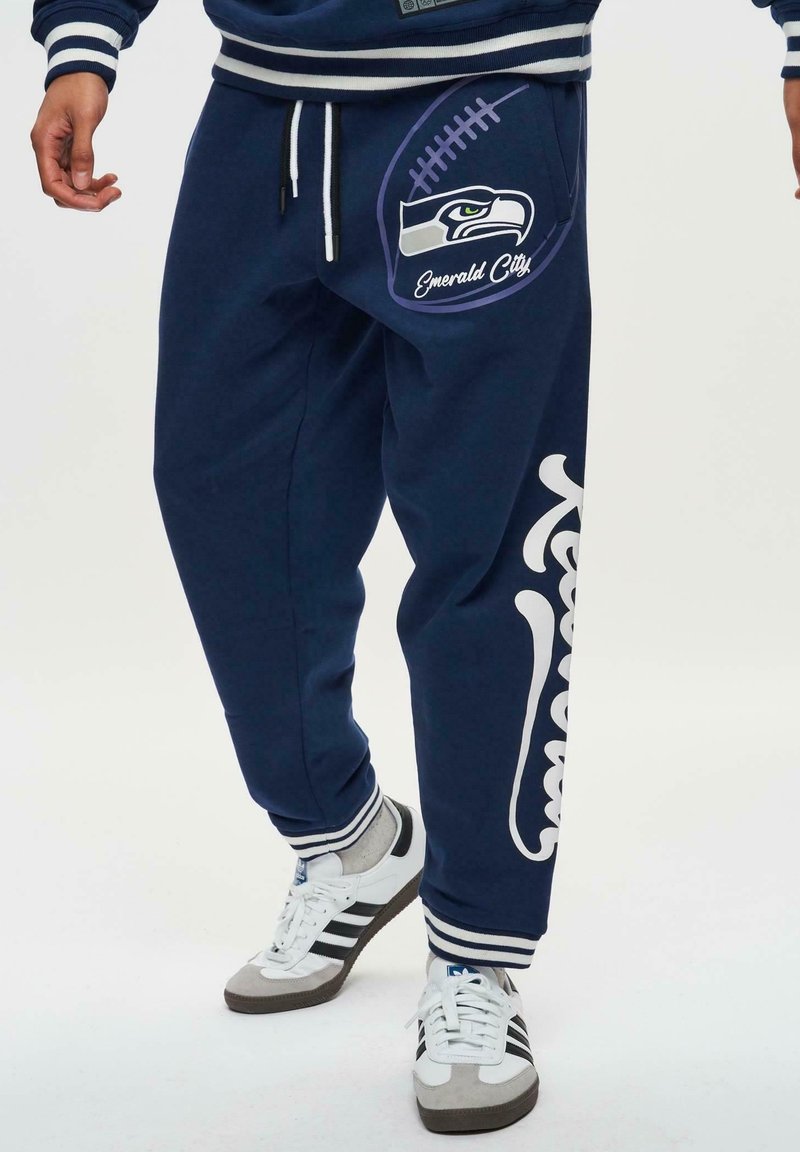 Marineblauwe sweatpants met een wit grafisch ontwerp van een voetbal en "Emerald City", elastische tailleband, geribbelde enkels en contrasterende witte randen.