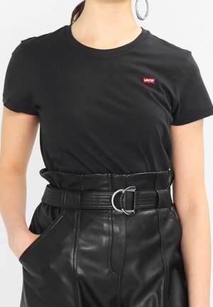 Musta puuvillainen t-paita, jossa pyöreä kaula-aukko ja pieni punainen Levi's-logo rinnassa, yhdistetty korkeavyötäröisiin mustiin nahkahousuihin, joissa on vyö.