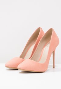 Talons aiguilles en suede pêche avec un bout pointu, finition lisse et un talon fin de 10 cm. L'intérieur est doté d'une doublure beige clair.