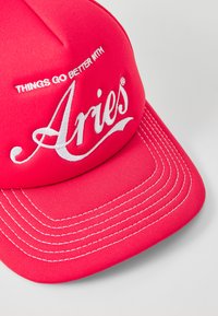 Red cap made of fabric, featuring white embroidered text "Aries" and a slogan above it. The bill has white stitching accents.