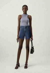 Ανοιχτό μωβ πλεκτό τοπ, τζιν σορτσάκια με ψηλή μέση και μαύρες σανδάλια με τετράγωνη φτέρνα. Το μοντέλο κρατάει μια μικρή μαύρη τσάντα.