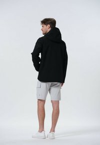 Svart huva jacka med l�ånga ärmar, kombinerad med ljusgrå cargo shorts. Modellen har på sig vita sneakers och visar en avslappnad outfit.