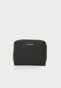 Svart dragkedja plånbok gjord av slätt material, med en silverfärgad Calvin Klein-logga på framsidan och en kompakt rektangulär form.