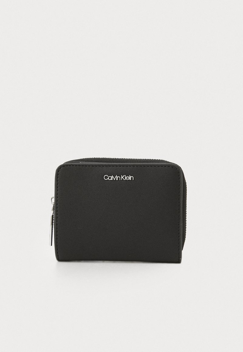 Svart dragkedja plånbok gjord av slätt material, med en silverfärgad Calvin Klein-logga på framsidan och en kompakt rektangulär form.