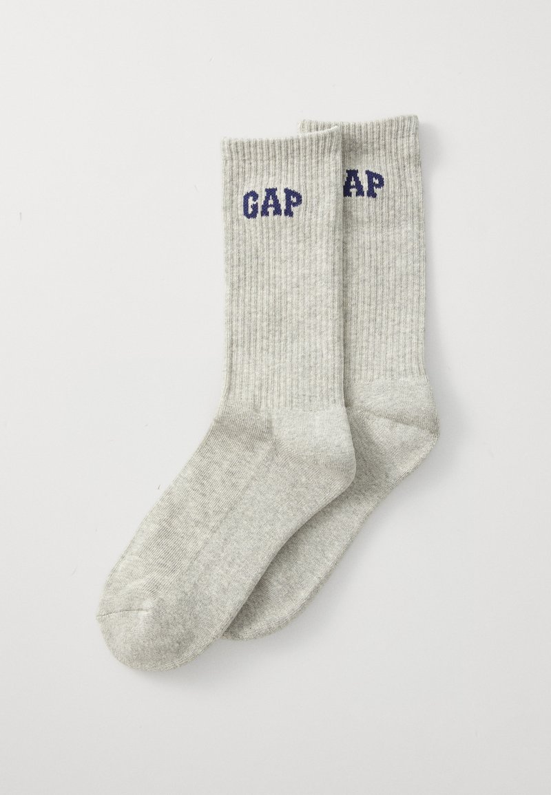 Calcetines de crew de tejido acanalado en gris claro con el logotipo oscuro de "GAP" cerca del puño, colocados en una superficie blanca.