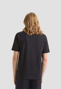 T-shirt nero a maniche corte con collo rotondo, texture liscia e un piccolo dettaglio ricamato sulla spalla sinistra sul retro.