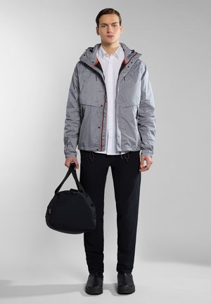 Gray and white checkered lightweight jacket with a hood, black pants, and a black duffel bag. Jacket features red accents and elastic drawstrings.