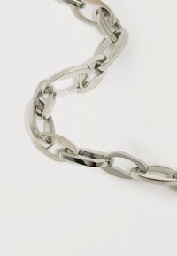 Metāla ķēdes kaklarota ar pagarinātiem, ovāliem posmiem, apstrādāta ar spīdīgu sudraba apdari, demonstrējot gludu tekstūru un savstarpēji savienotu dizainu.