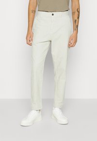 Ljusbeige chinos med rak passform, tillverkade av mjukt tyg. Har knappstängning, sidofickor och är kombinerade med vita sneakers.