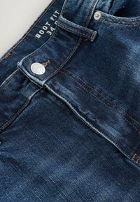 Tumšo zilu džinsu bikses ar pieguļošu griezumu, gludu tekstūru, kontrastējošiem brūniem diegiem un metāla pogu jostasvietā. Izmērs 34.